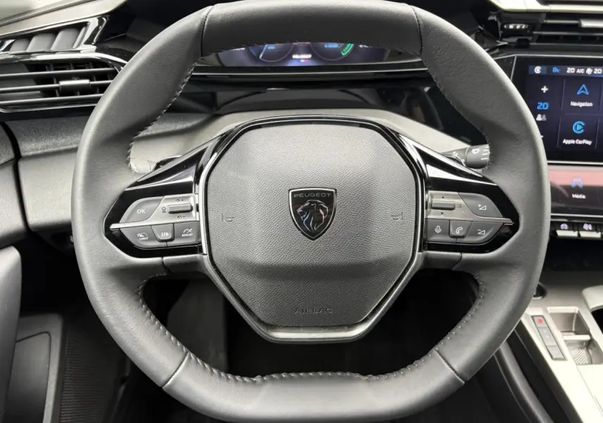 Gros plan sur le volant cuir noir du Peugeot 308 SW Hybrid 2025 avec commandes intégrées et tableau de bord numérique.
