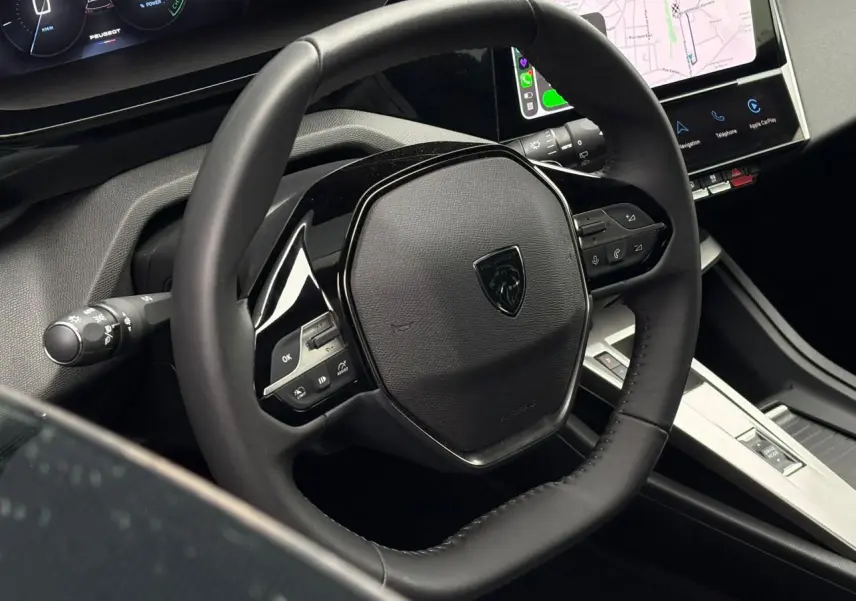 Vue rapprochée du volant en cuir noir et de l'écran tactile central du Peugeot 308 SW Hybrid 2025.
