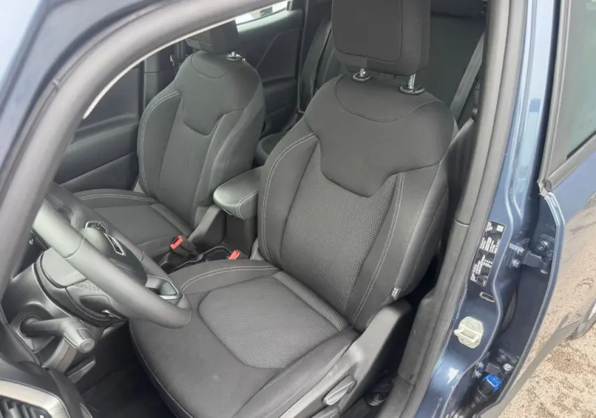 Vue intérieure côté conducteur du Jeep Renegade 2024 bleu, avec sièges tissu noirs et accoudoir central visible.