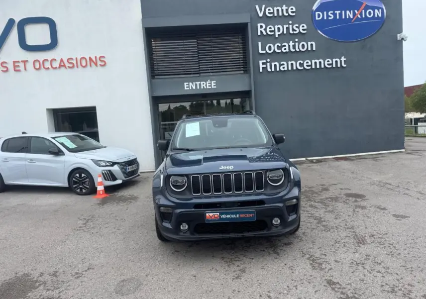Jeep Renegade bleu vue de face, avec calandre à sept fentes et phares ronds, stationné devant un bâtiment commercial.