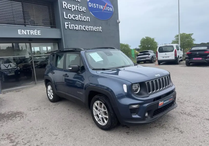 Jeep Renegade bleu en 3/4 avant droit, avec barres de toit et jantes alliage 17 pouces, stationné devant un concessionnaire.