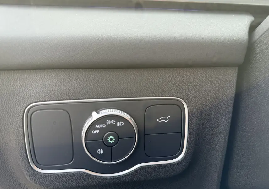 Gros plan sur le bouton de commande des phares et ouverture du coffre intérieur du JAECOO J5 gris Phantom.