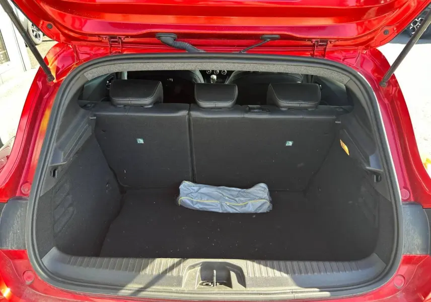 Coffre ouvert vue arrière d'une Renault Clio Rouge Flamme 2025, banquette arrière noire et tapis de coffre vide.
