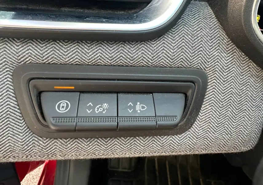 Panneau de commandes noires sur tissu gris à chevrons dans Renault Clio Rouge Flamme, réglages éclairage et verrouillage portes.