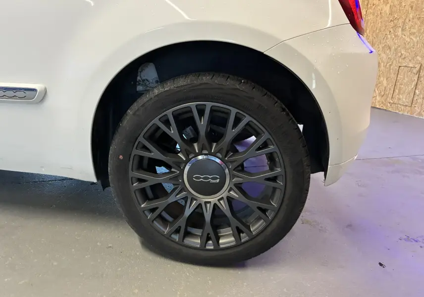 Gros plan sur la roue arrière droite d'une FIAT 500 blanche de 2021 avec jante noire au design ajouré.