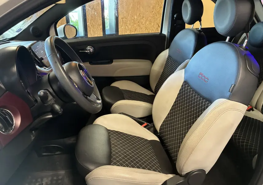 Vue intérieure côté conducteur de la Fiat 500 blanche 2021, sièges bi-ton noir et beige avec logo 500 brodé.