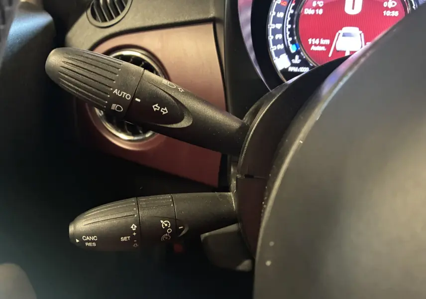 Gros plan sur les commandes de clignotants et régulateur de vitesse à gauche du volant d'une Fiat 500 blanche, tableau de bord partiellement visible.