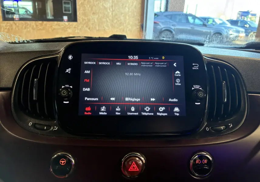 Vue rapprochée de l’écran tactile central du tableau de bord de la Fiat 500 blanche, affichant la radio FM.