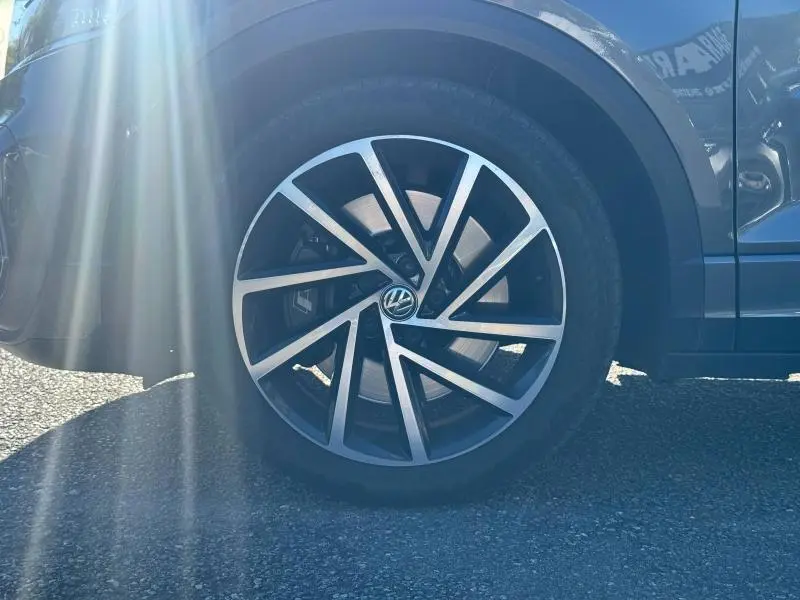 Gros plan sur la roue avant gauche noire avec jante alliage argentée et logo Volkswagen au centre, sur carrosserie sombre.