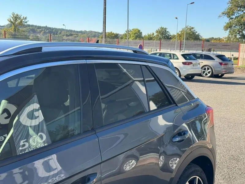 Vue latérale droite du Volkswagen T-Roc gris métallisé, mettant en valeur les vitres teintées et barres de toit.