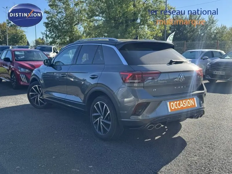 Volkswagen T-Roc gris métallisé vu en 3/4 arrière droit avec jantes alu et double sortie d’échappement chromée.