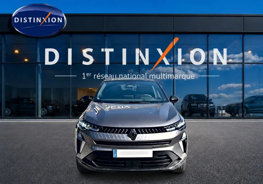 Vue frontale d'un Renault Captur gris cassiopée 2026, avec calandre moderne et phares LED allumés, devant une vitrine Distinxion.