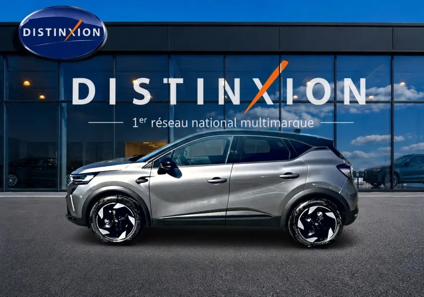 Profil droit d'un Renault Captur gris cassiopée 2026, avec jantes alu noires et toit noir, devant une vitrine Distinxion.