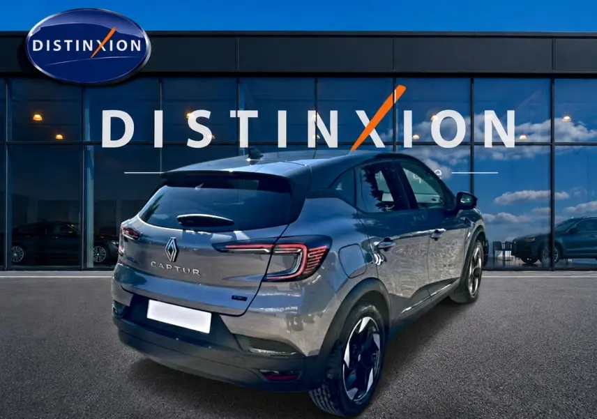 Vue 3/4 arrière droite d'un Renault Captur gris cassiopée 2026 devant une vitrine avec logo Distinxion.