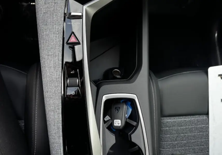 Gros plan sur la console centrale du Peugeot 5008 III avec clé, finition tissu gris et cuir noir.