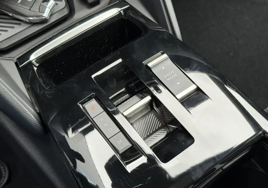 Gros plan sur la console centrale noire brillante de la Citroën C4 NV Hybrid 2025 avec commandes de boîte auto et mode de conduite.