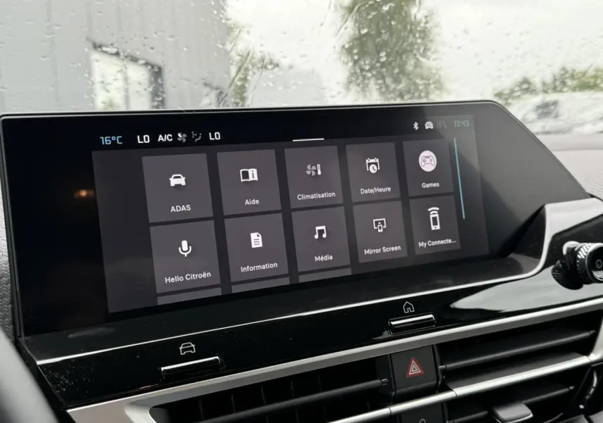 Écran tactile central du tableau de bord du Citroën C4 blanc, affichant le menu principal sous la pluie.