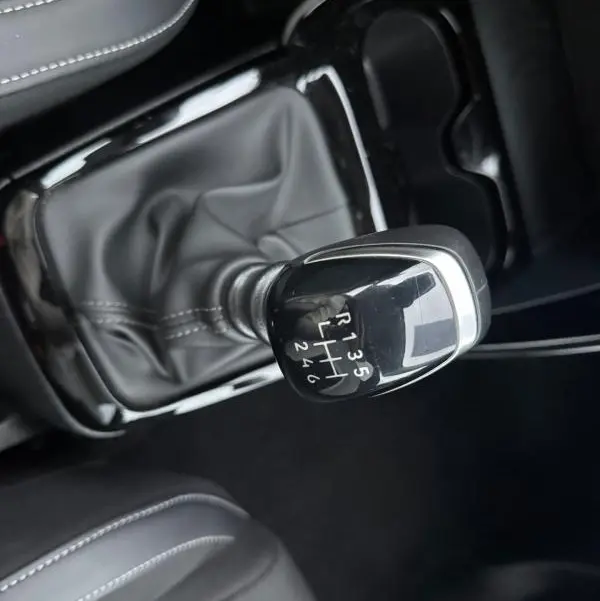 Gros plan sur le levier de vitesse manuel noir de la Citroën C3 gris, entouré de sellerie noire avec surpiqûres blanches.