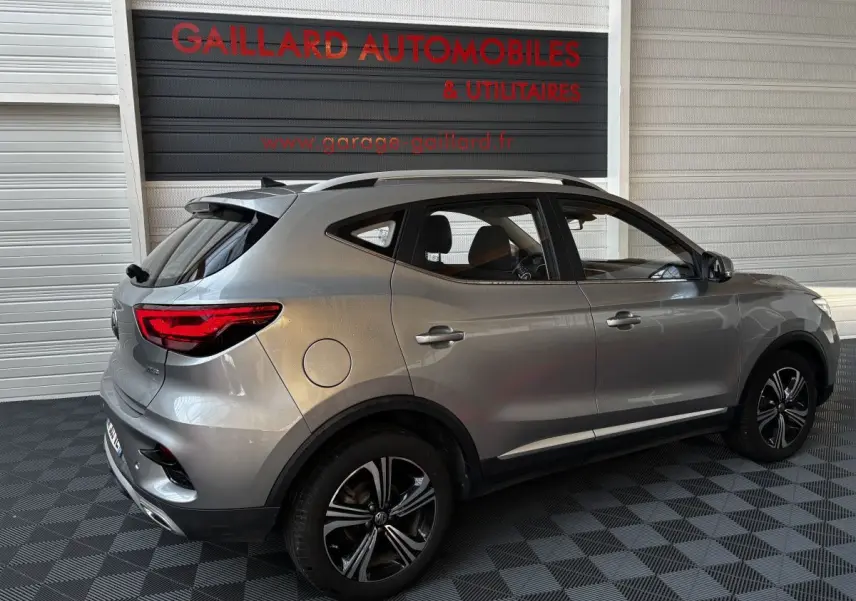 Vue 3/4 arrière côté droit d’un SUV MG ZS gris clair 2022 avec jantes alliage et feux arrière LED allumés.
