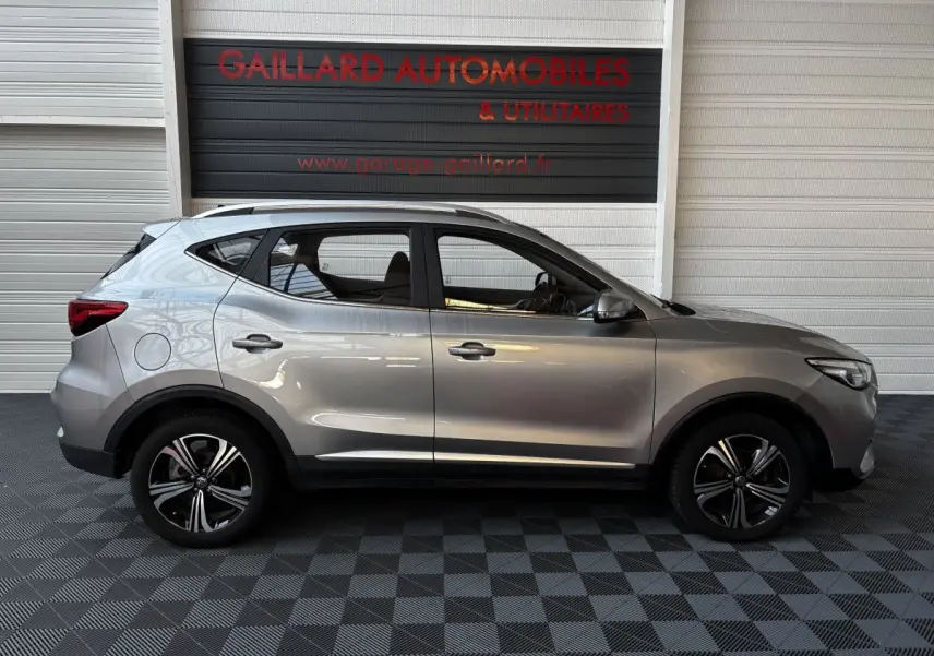Vue de profil côté gauche d’un MG ZS gris clair 2022, SUV compact avec jantes alliage et barres de toit chromées.