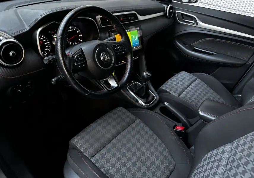 Vue intérieure côté conducteur du MG ZS 2022, volant cuir, sièges tissu gris à motifs, écran tactile central allumé.