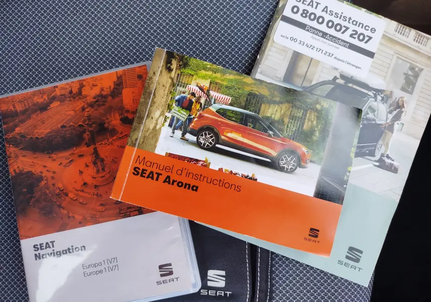 Vue latérale droite d'un SEAT Arona orange sur un manuel d'instructions posé sur un tissu gris.
