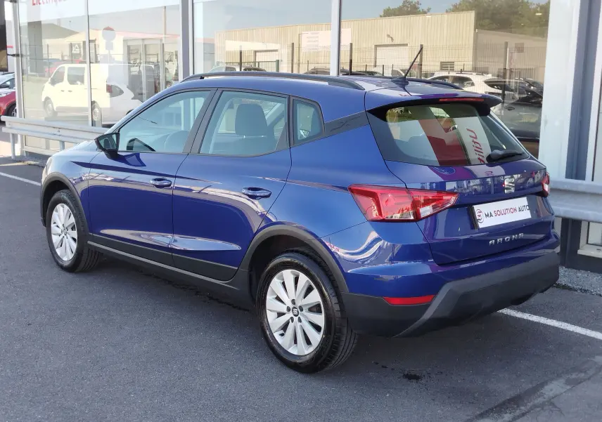 SEAT Arona bleu électrique vu en 3/4 arrière côté gauche, avec jantes argentées et feux arrière distinctifs.