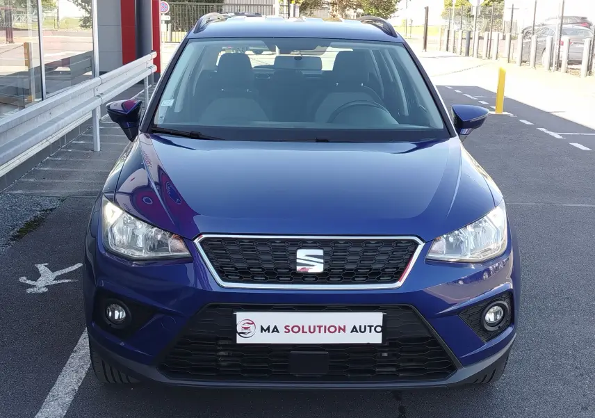 Vue frontale d'un SEAT Arona bleu électrique 2019 avec calandre noire et phares allumés en extérieur.