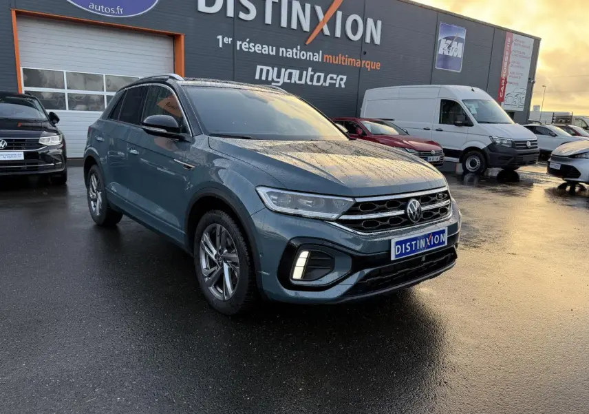 Volkswagen T-Roc bleu pétrole métallisé en 3/4 avant droit sous la pluie avec jantes alliage et feux LED allumés.