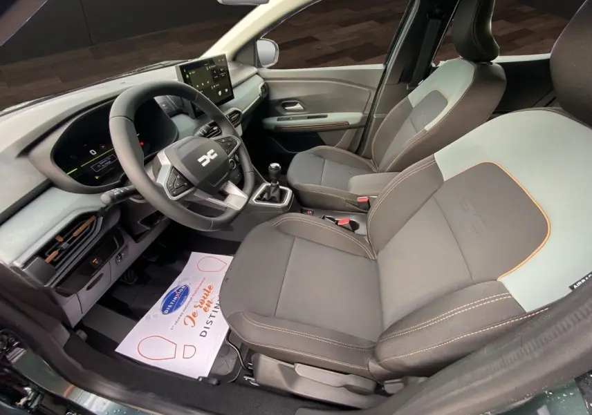 Vue intérieure côté conducteur de la Dacia Sandero Stepway 2026 avec sièges tissu gris noir et tableau de bord moderne.