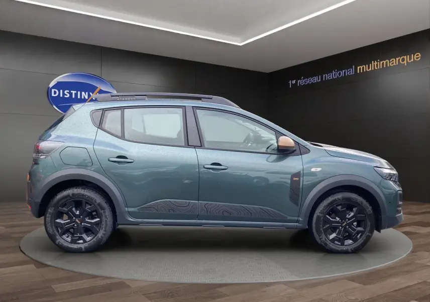 Vue de profil côté gauche d'une Dacia Sandero Stepway 2026 vert cèdre avec jantes alliage noires et barres de toit.