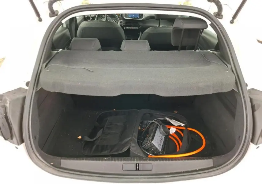Vue arrière du coffre ouvert d'une Peugeot 208 électrique blanche avec câble de recharge visible à l'intérieur.