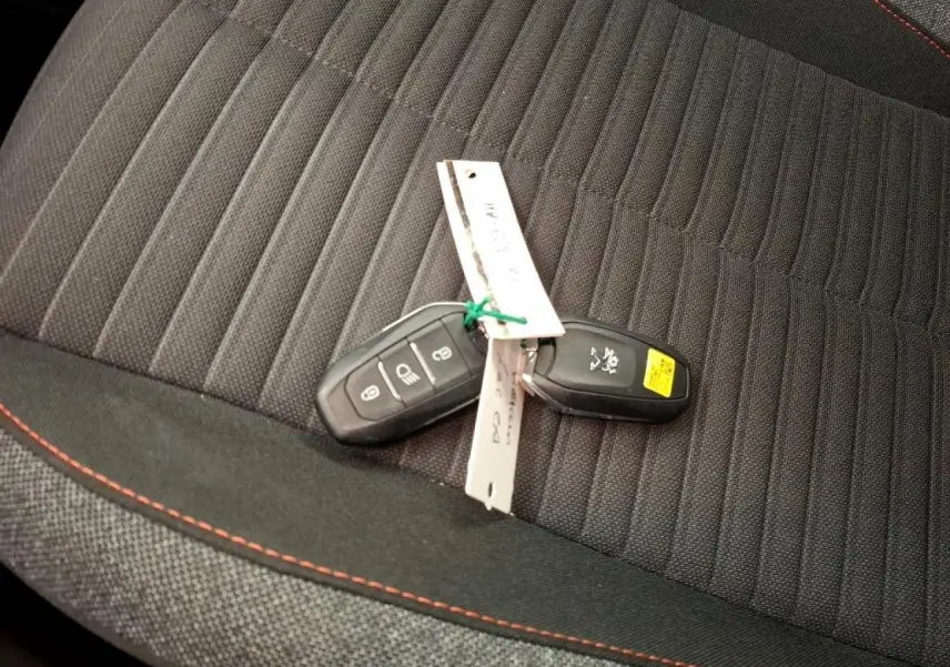 Clé de voiture Peugeot posée sur siège tissu noir avec surpiqûres orange, vue rapprochée intérieure.