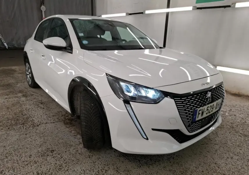 Peugeot 208 électrique blanc banquise vue 3/4 avant droit avec phares LED allumés en intérieur.