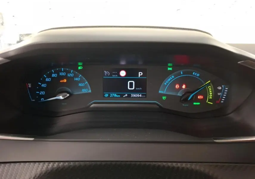 Vue rapprochée du combiné d'instruments numérique de la Peugeot 208 e-136 blanche, affichant 0 km/h et 27 8 km d'autonomie.