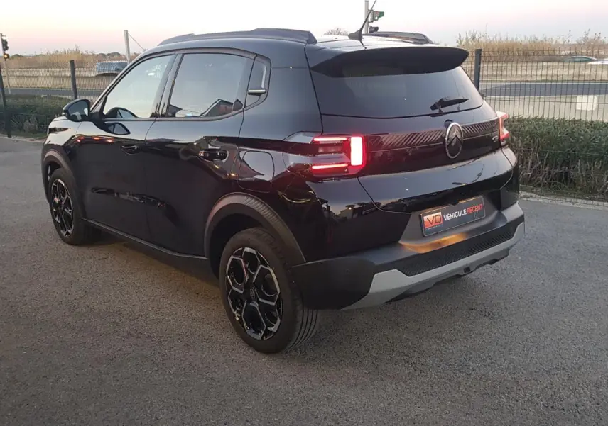 Vue 3/4 arrière droite d'une Citroën C3 noire 2025 avec jantes alliage 17 pouces et barres de toit.