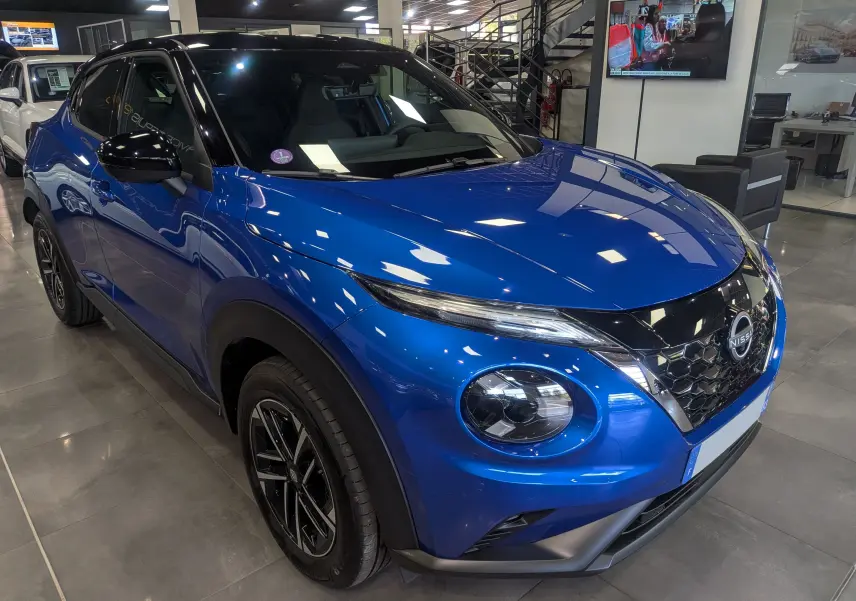 Vue 3/4 avant droit du Nissan Juke Hybrid 2025 en bleu magnétique avec toit noir et jantes noires en concession.