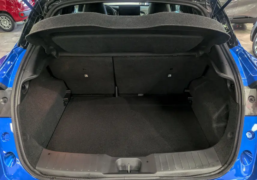 Coffre ouvert vu de l'arrière d'un Nissan Juke Hybrid 2025 bleu magnétique avec toit noir, intérieur de coffre vide et propre.
