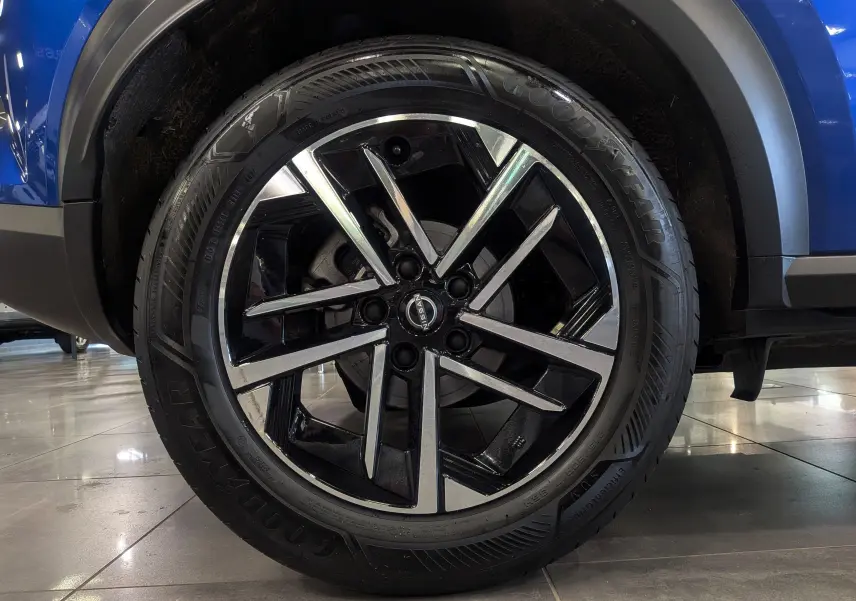 Gros plan sur la roue avant droite du Nissan Juke Hybrid bleu magnétique, jante alliage noir et argentée au design moderne.