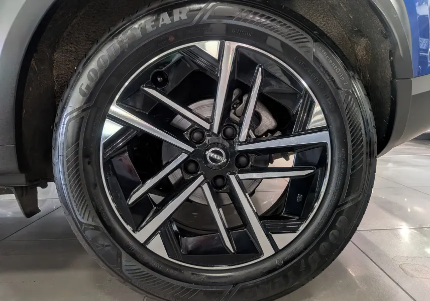 Gros plan sur la roue avant droite du Nissan Juke Hybrid 2025 bleu magnétique, jante alliage noir et argentée.