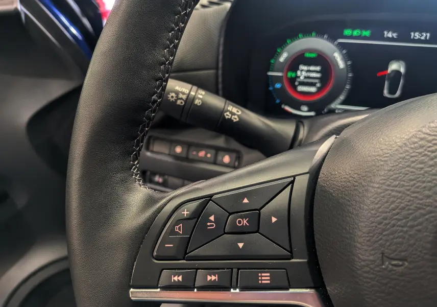 Gros plan sur le volant en cuir noir du Nissan Juke Hybrid 2025, avec commandes multifonctions et tableau de bord numérique en arrière-plan.