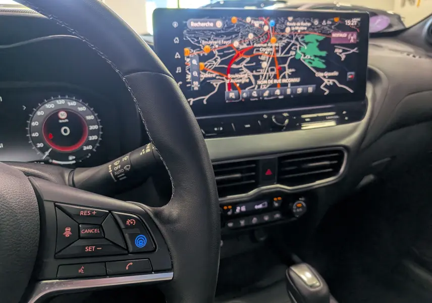 Vue intérieure du tableau de bord du Nissan Juke Hybrid 2025, avec écran tactile de navigation et volant multifonction en cuir noir.