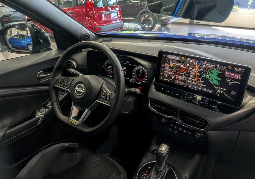 Vue intérieure côté conducteur du Nissan Juke Hybrid 2025, avec tableau de bord numérique et écran tactile de navigation.