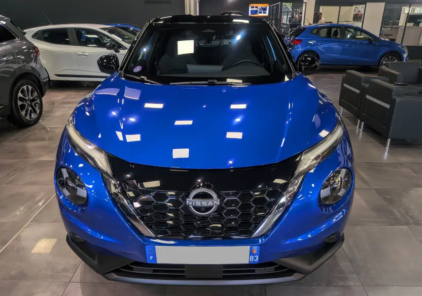 Vue frontale d'un Nissan Juke 2025 bleu magnétique avec toit noir, mettant en valeur sa calandre hexagonale distinctive.