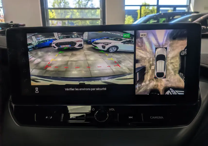 Écran intérieur du Nissan Juke Hybrid 2025 montrant la caméra de recul et la vue 360° avec le véhicule en bleu magnétique et toit noir.