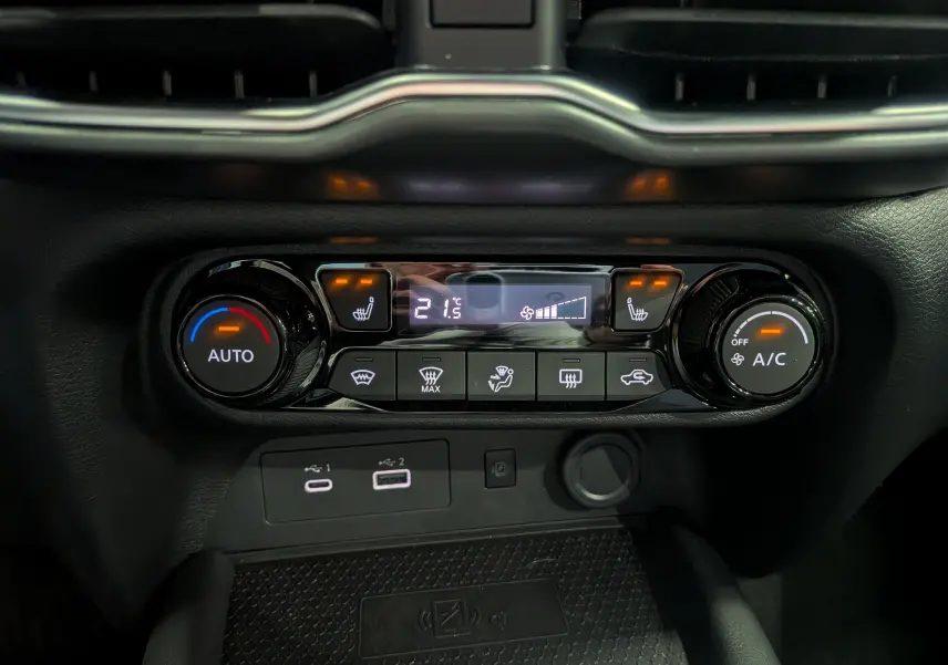 Gros plan sur la console centrale du Nissan Juke Hybrid 2025, montrant les commandes de climatisation et les ports USB.