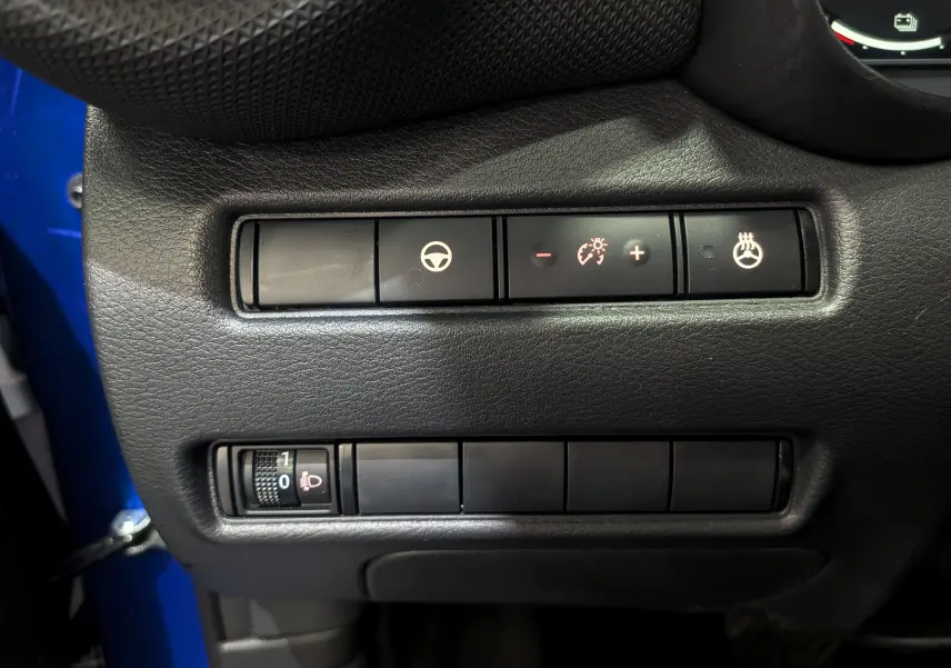 Gros plan sur les commandes de réglage du volant, éclairage et siège chauffant du Nissan Juke bleu magnétique 2025.