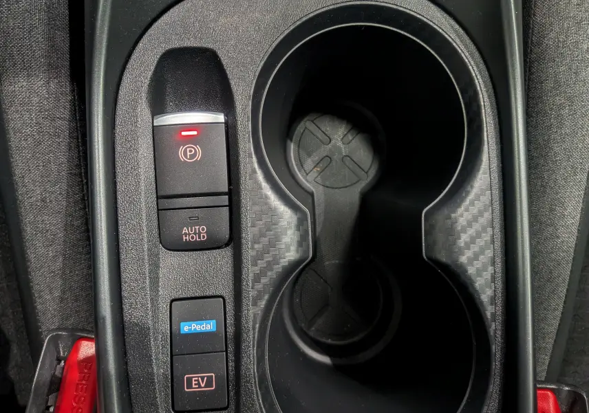 Vue rapprochée de la console centrale du Nissan Juke Hybrid 2025 avec boutons e-Pedal, EV et frein de parking électrique.