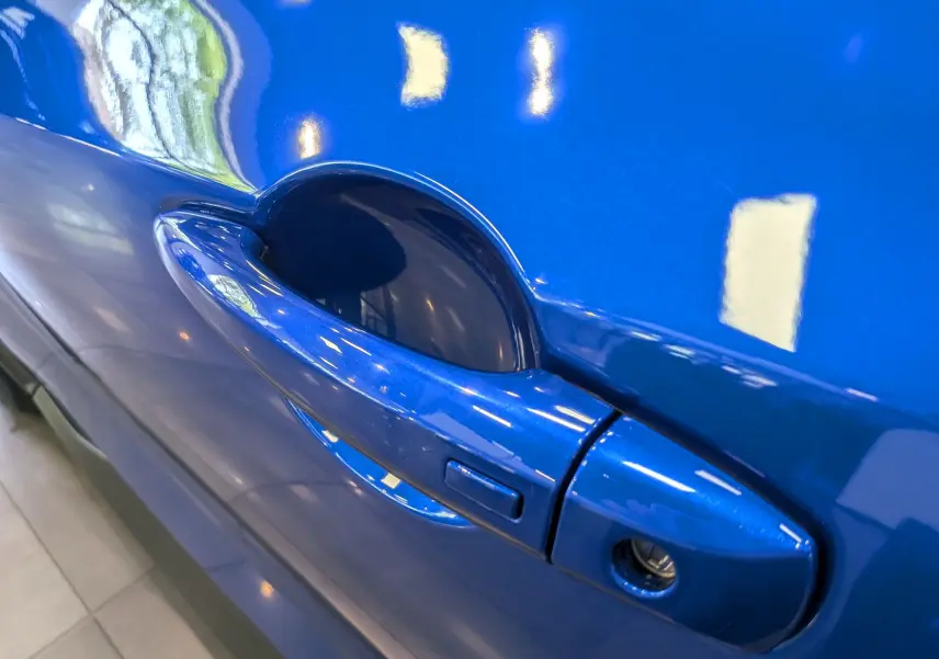 Gros plan sur la poignée de porte côté gauche du Nissan Juke Hybrid 2025 en bleu magnétique avec toit noir.