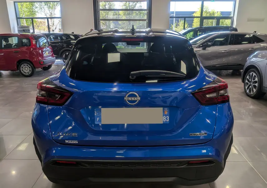 Vue arrière d’un Nissan Juke Hybrid bleu magnétique avec toit noir, en intérieur de showroom lumineux.